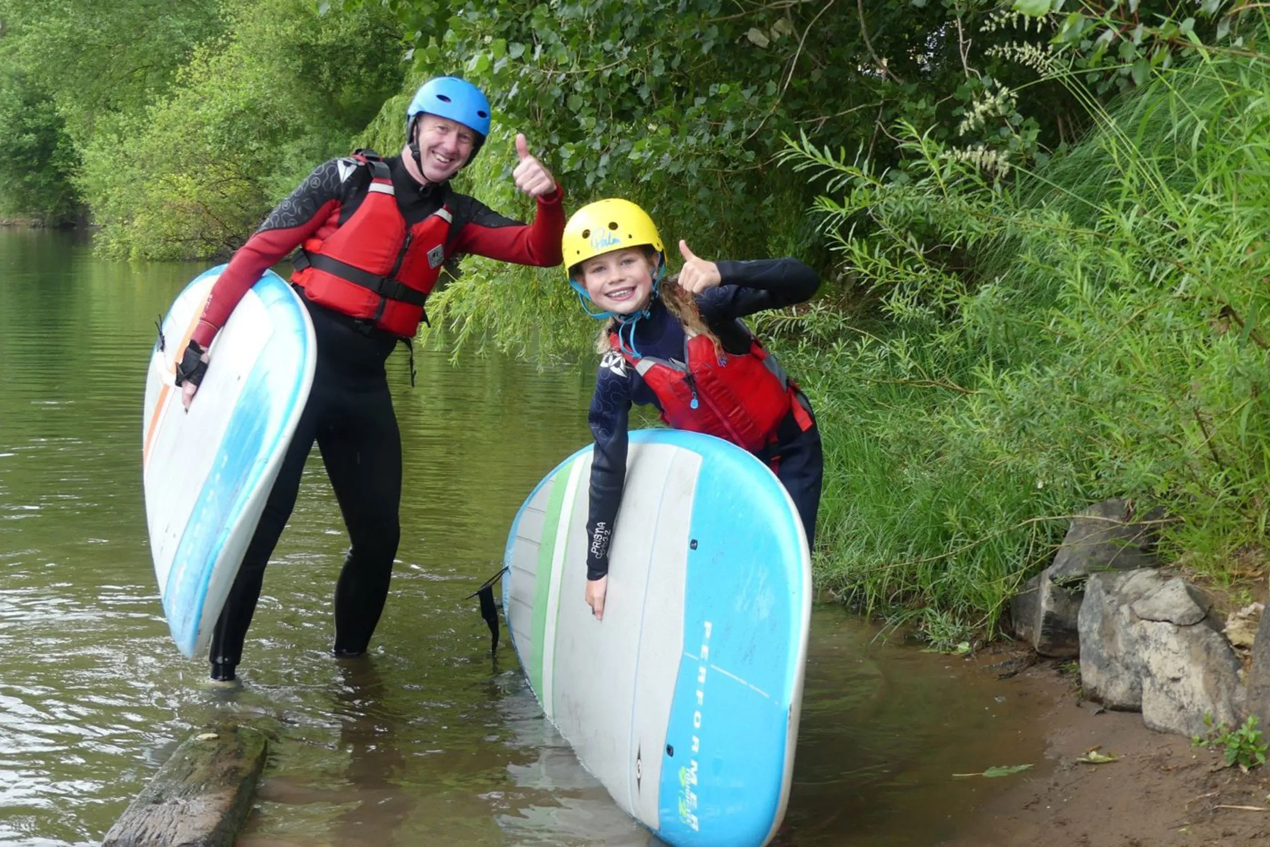 Two smiling people holding canoes giving thumbs up
